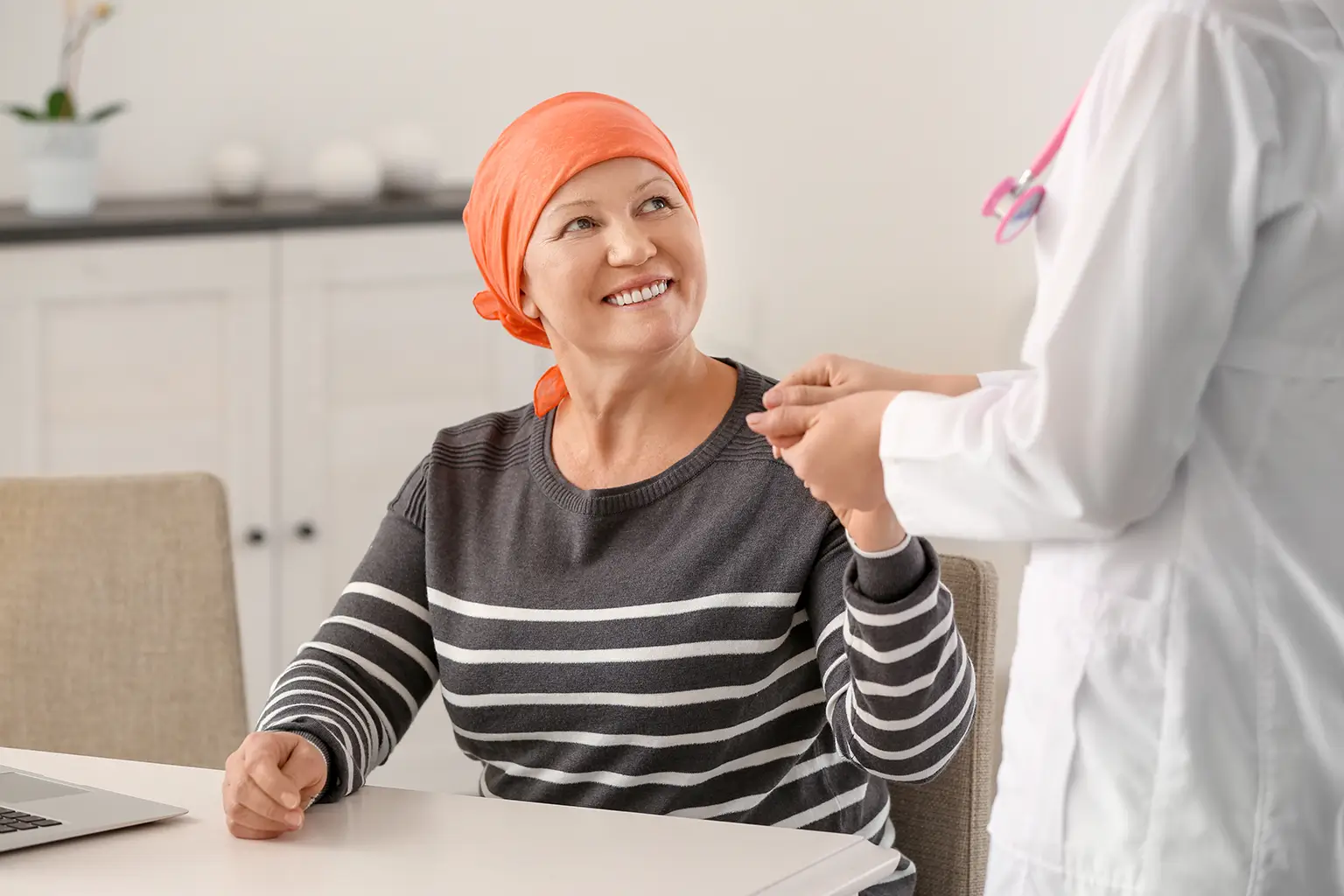 A Cancer Patient in an Orange Headscarf Smiles Warmly While Holding Hands with Her Doctor