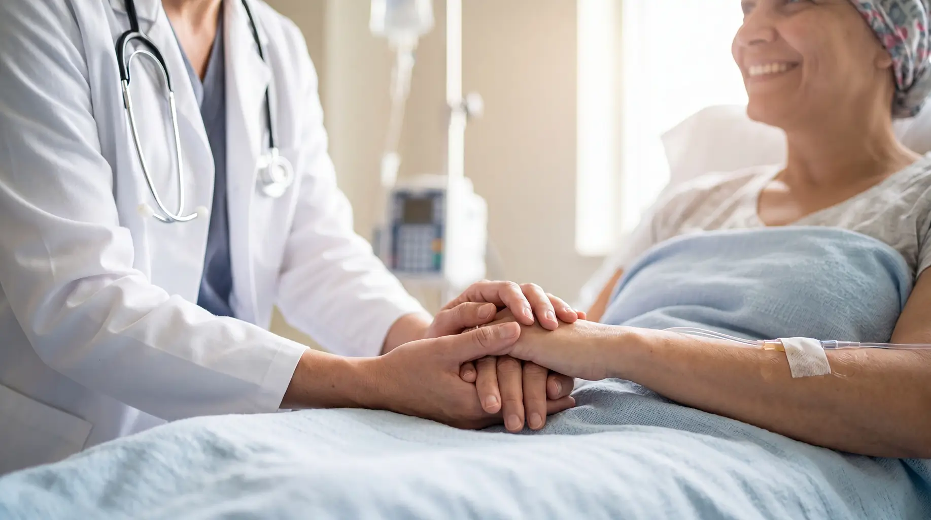 A Doctor Holding Hands With a Smiling Cancer Patient Resting in a Hospital Bed With an IV