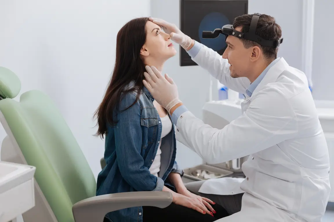 A doctor is checking a woman's thyroid during an ENT examination in a medical office.