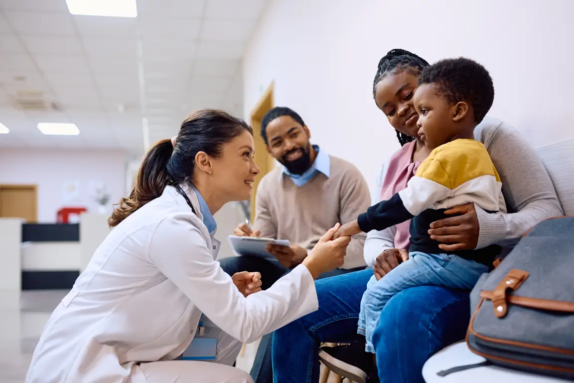 Pediatrician interacting with a young child and their parents in a waiting area.