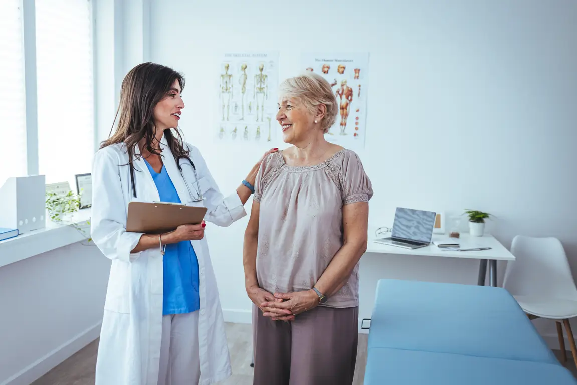Female doctor speaking to an older female patient in an exam room.